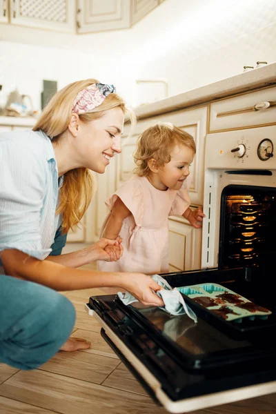 若い母親と子供はチョコレートペストリーとオーブンベーキングシートから削除します キッチンで女性と女の子の料理 ケーキの準備 幸せな家族はデザートを作る — ストック写真