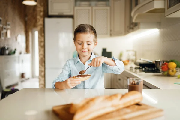 若い男の子はパンにチョコレートを溶かした キッチンで調理かわいい男の子 幸せな子供はカウンターで甘いデザートを準備し 味わいます — ストック写真