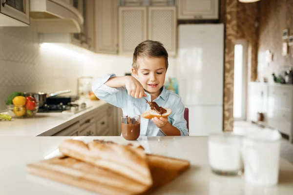 若い男の子はパンにチョコレートを溶かした キッチンで調理かわいい男の子 幸せな子供はカウンターで甘いデザートを準備し 味わいます — ストック写真