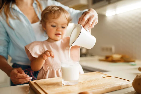 若い母と子供は ペストリーのための成分 ガラスにミルクを注ぎます キッチンで料理する女と小さな女の子 ケーキの準備 幸せな家族はカウンターで甘いデザートを作ります — ストック写真