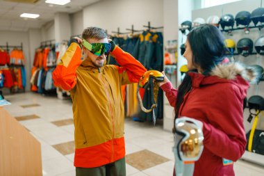 Vitrinde kayak veya snowboard için maske deneyen çift, spor mağazasında alışveriş. Kış sezonu aşırı yaşam tarzı, aktif eğlence mağazası, müşteriler gözlük satın alma, ekipman korumak