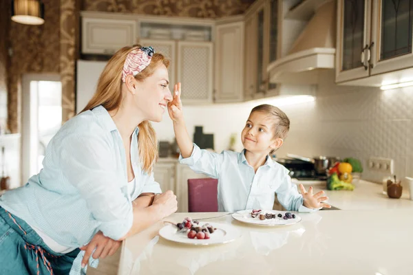 Young mother with her son tastes chocolate pastry. Cute woman and little boy cooking on the kitchen. Happy family tasting sweet dessert at the counter and having fun