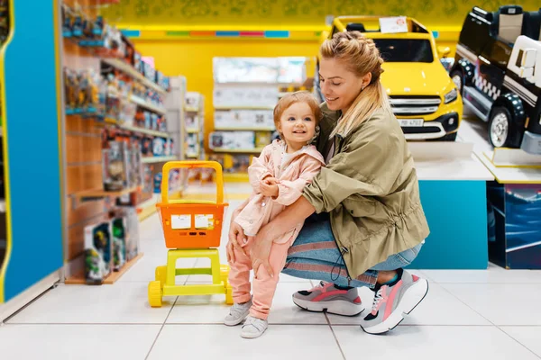 子供の店で小さな娘と幸せな母親 スーパーでおもちゃを選ぶママと子供 家族の買い物 — ストック写真