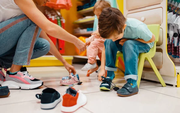 子供の店で靴を選ぶ彼女の小さな子供を持つ母 一緒にスーパーマーケットで服を買う娘と息子と幸せなママ 家族の買い物 — ストック写真