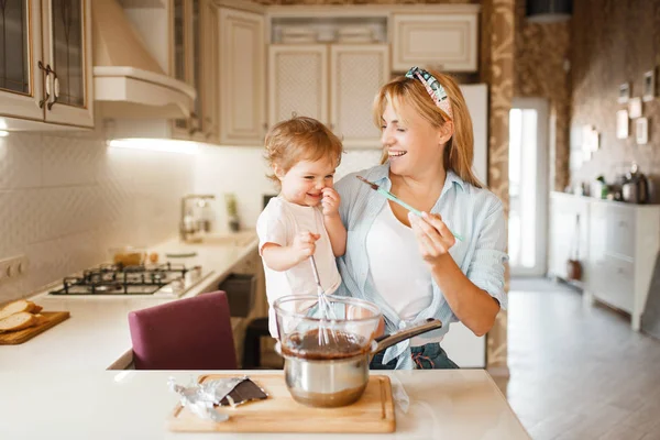 娘と一緒に若い母親が溶かしたチョコレートをボウルに入れて混ぜます 台所でかわいい女性と女の子の料理 幸せな家族は甘いデザートを準備します — ストック写真