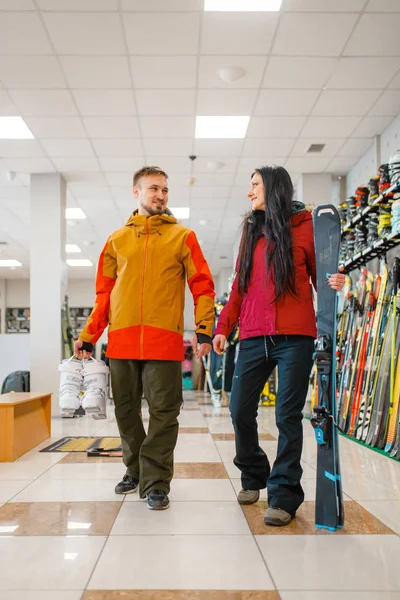 Couple with skis and boots in hands, shopping in sports shop. Winter season extreme lifestyle, active leisure store, customers buying skiing equipment