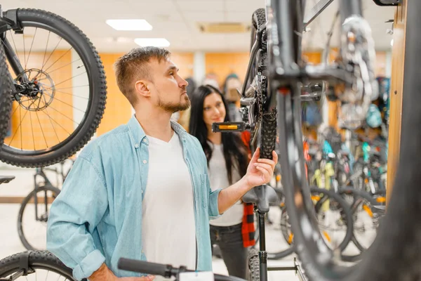 Man checks bicycle disk breaks, shopping in sports shop. Summer season extreme lifestyle, active leisure store, customers buying cycle, couple choosing bikes