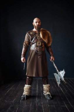 Geleneksel İskandinav kıyafetleri giymiş baltalı Viking. Antik savaşçı, arka planda siyah duvarlar ve ahşap zemin ile stüdyo