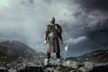 Kayalık dağlarda duran geleneksel İskandinav giysileri giymiş balta ile Viking. İskandinav antik savaşçı