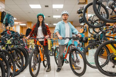 Couple in cycling helmets choosing bicycles, shopping in sport shop. Summer season extreme lifestyle, active leisure store, customers buying cycles clipart