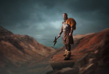 Kayalık dağın tepesinde duran geleneksel İskandinav giysileri giymiş balta ile Yakışıklı viking. İskandinav antik savaşçı