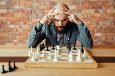 Erkek satranç oyuncusu siyah figürler, düşünme süreci oynuyor. Satranç oyuncusu gemide, entelektüel turnuva kapalı. Ahşap masa üzerinde Satranç Tahtası, strateji oyunu