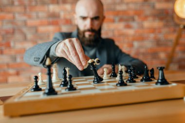 Erkek satranç oyuncusu, beyaz figürü hareket, siyah kraliçenin kaybı. Gemide chessplayer, ön görüş, entelektüel turnuva kapalı. Ahşap masa üzerinde chessboard, strateji oyunu