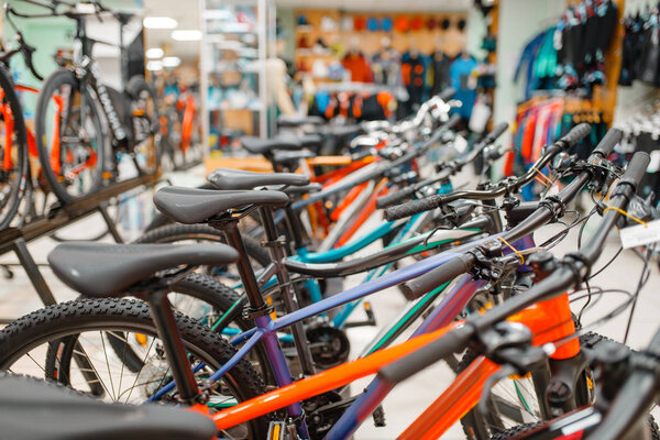 Rows of mountain bicycles in sports shop, focus on seat, nobody. Summer active leisure, showcase with bikes, cycle sale