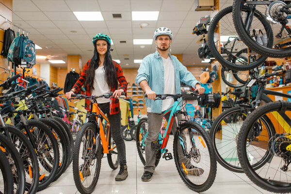 Couple in cycling helmets choosing bicycles, shopping in sport shop. Summer season extreme lifestyle, active leisure store, customers buying cycles