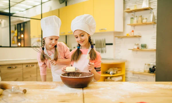 2人の小さな女の子がキャップで調理し ボウルにバターを追加し キッチンでクッキーの準備 子供たちはペストリーを調理し 子供のシェフは生地を作り 子供はケーキを準備します — ストック写真