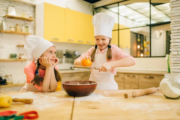 2人の小さな女の子がボウルにオレンジ色をこすり 台所でクッキーの準備をキャップで調理します 子供たちはペストリーを調理し ケーキを準備する子供のシェフ — ストック写真