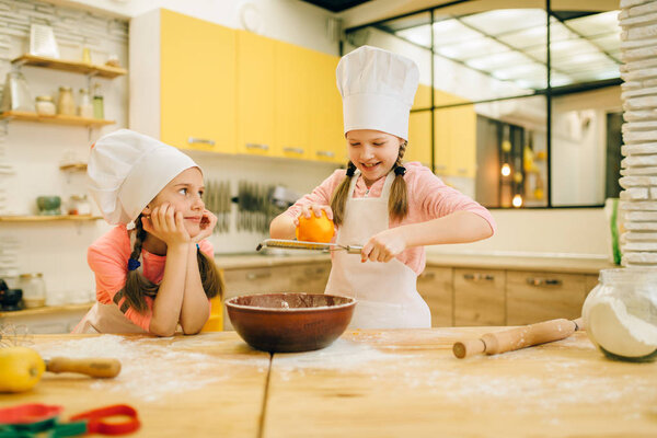Две маленькие девочки готовят в шапочках, натирают апельсином миску, готовят печенье на кухне. Дети готовят выпечку, дети готовят торт
