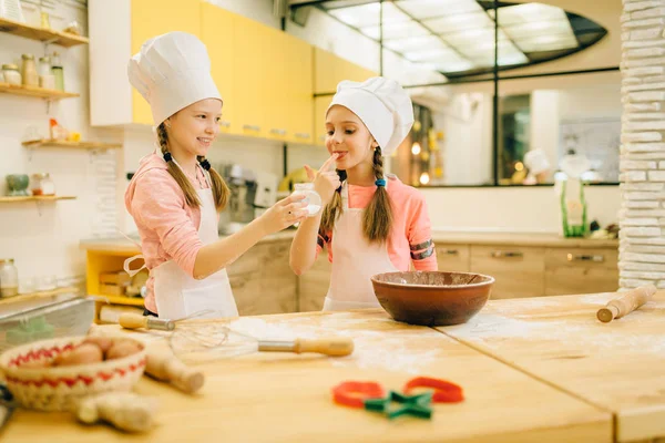 キャップで調理する2人の小さな女の子は甘いバニラパウダー キッチンでクッキーの準備を味わいます 子供たちはペストリーを調理し ケーキを準備する子供のシェフ — ストック写真