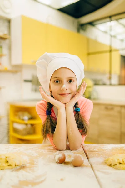 キャップとエプロンで小さな女の子の料理は キッチンで混合 クッキーの準備のための泡立て器を保持しています 子供たちはペストリーを調理し ケーキを準備する子供のシェフ — ストック写真