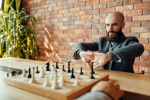 Erkek satranç oyuncuları yarışmada, rakamlarla tahtaya. İki satranç oyuncusu entelektüel turnuvaya kapalı mekanlarda başlar. Ahşap masa üzerinde Satranç Tahtası, strateji oyunu