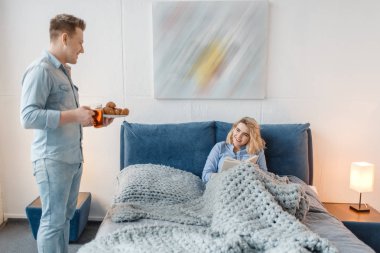 Aşk çift kruvasan ve kurabiye ile yatakta romantik kahvaltı yapıyor. Erkek ve kadın yatak odasında tatlı yer, günaydın. Mutlu yaşam tarzı, güzel bir ilişki