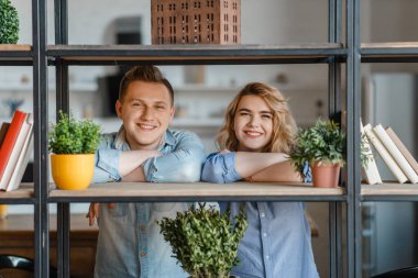 Ev bitkileri, çiçekçi hobi ile rafta genç gülümseyen çift. Erkek ve kadın ilgilenir ve ev çiçekleri büyüyen, bahçe, botanik yaşam tarzı