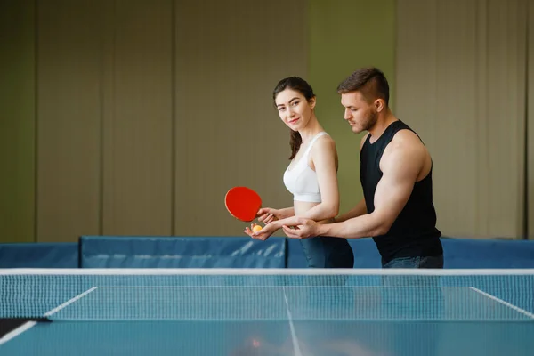 남자는 실내에서 탁구를 훈련을 여자를 가르칩니다 스포츠웨어의 커플은 라켓을 체육관에서 — 스톡 사진