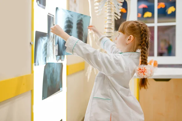 制服を着た小さな女の子は プレイルームを再生し X線を見ます 子供は架空の病院で医療従事者を演じる 職業学習 ストック写真