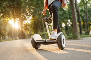 Yaz parkında jiroboard'a binen genç erkek. Elektrikli gyro tahtası ile açık hava rekreasyon. Denge teknolojisi ile eko ulaşım. Elektrikli jiroskop araç
