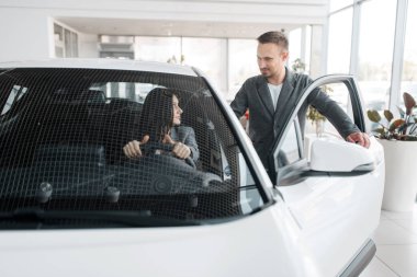 Showroom'da yeni araba alan mutlu çift, direksiyonbaşındaki kadın. Bayilik, otomobil satışı araç seçiminde erkek ve kadın müşteriler