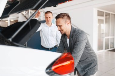 Alıcı ve yönetici showroom yeni arabanın bagajına bakar. Bayilik, otomobil satışı, oto satın alma araç seçimi erkek müşteri