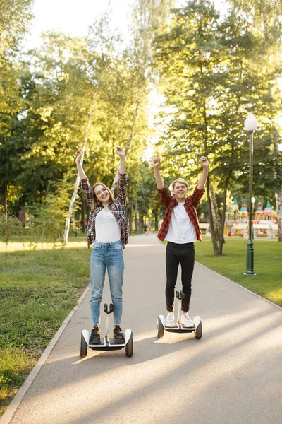 年轻的幸福夫妇骑在陀螺板在夏季公园 带电动陀螺板的户外休闲活动 环保运输与平衡技术 电动陀螺仪车辆 — 图库照片