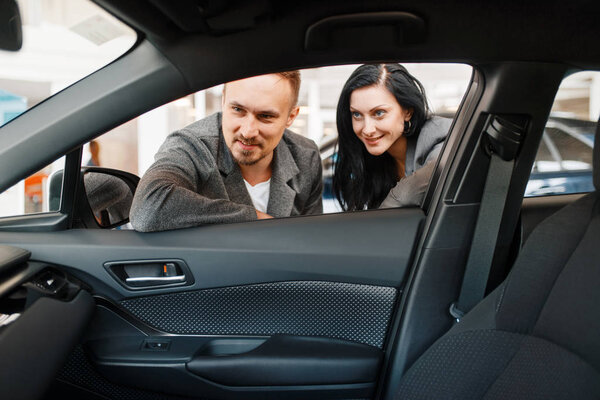 Пара взглядов на интерьер нового автомобиля в выставочном зале. Мужчины и женщины покупают автомобиль в автосалоне, продают автомобиль, покупают автомобиль
