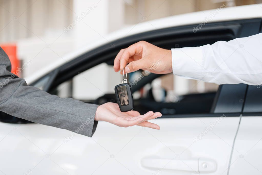 Manager gives to woman the key to the new car in showroom. Female customer buying vehicle in dealership, automobile sale