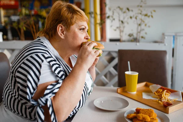 モールフードコートでハンバーガーを食べる太った女性 ジャンクランチ 肥満問題でテーブルで太りすぎの女性 — ストック写真