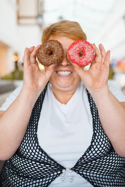 モールレストランで目の代わりにドーナツを持つ太った女性 不健康な食べ物 ジャンクディナー 肥満の問題でテーブルで太りすぎの女性 — ストック写真