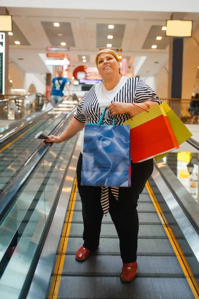 在商场的自动扶梯上装着购物袋的胖女人 超市超重女性 高脂肪购物狂 肥胖问题 — 图库照片