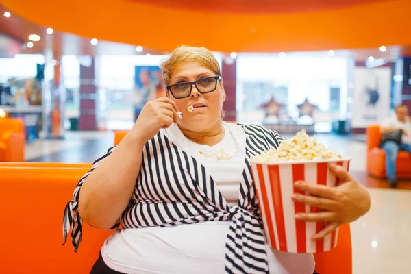 Fatty woman eating popcorn in the cinema hall, unhealthy junk food. Overweight female person in mall, obesity problem