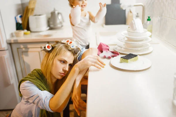 Ένα Κοριτσάκι Που Πλένει Πιάτα Κοντά Μια Κουρασμένη Νοικοκυρά Γυναίκα — Φωτογραφία Αρχείου