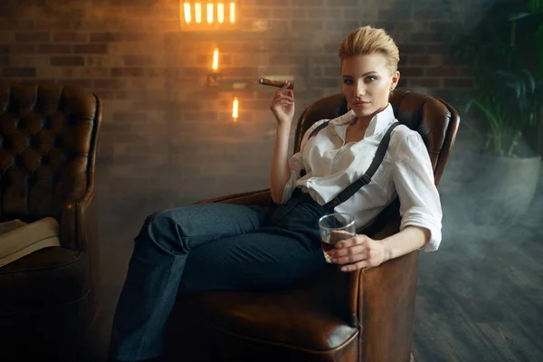 ウィスキーやシガー レトロなファッション ギャングのスタイルで革の椅子に座ってシャツやズボンの女性 レンガの壁を持つオフィスのヴィンテージビジネス女性 — ストック写真