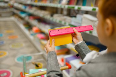 El arabasıyla not defteri seçen, kırtasiyeden alışveriş yapan küçük bir kız öğrenci. Kadın çocuk dükkandan ofis malzemeleri alıyor, okul çocuğu da süpermarketten.