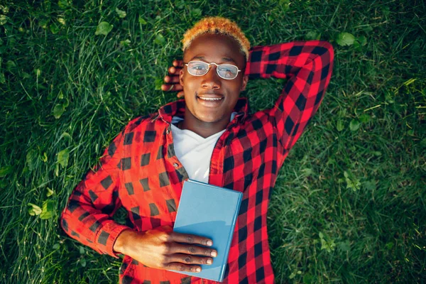 夏の公園で草の上の本を読んでいるアフリカの学生 — ストック写真