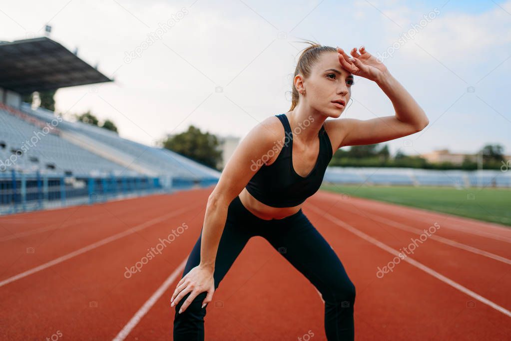 Tired female jogger in sportswear, training on stadium. Woman doing stretching exercise before running on outdoor arena