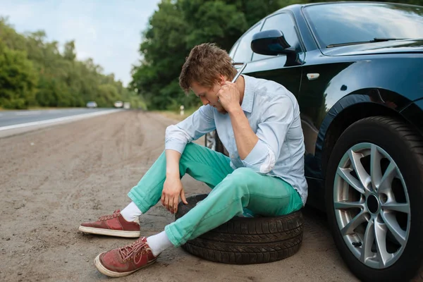 车坏了 年轻人坐在备胎上 汽车故障或车辆故障 公路上汽车轮胎爆胎故障 — 图库照片