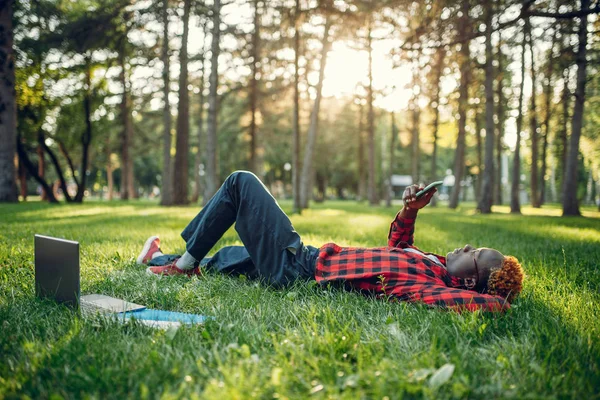 Afrykański Student Telefonem Leżącym Trawie Letnim Parku — Zdjęcie stockowe