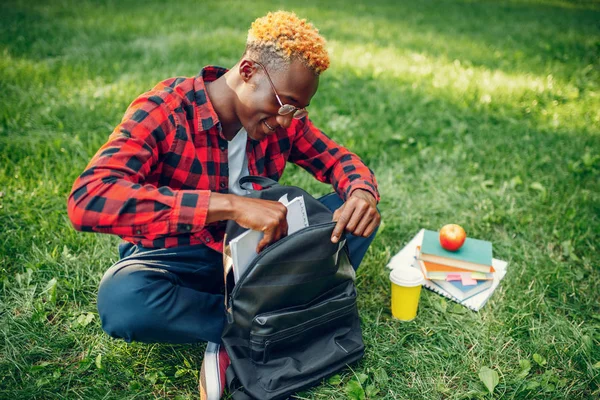 夏の公園で草の上に座ってリュックを持つ黒の学生 屋外で勉強して昼食をとる10代 — ストック写真