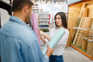 Young couple choosing wallpapers color in hardware store. Male and female customers look at the goods in diy shop clipart