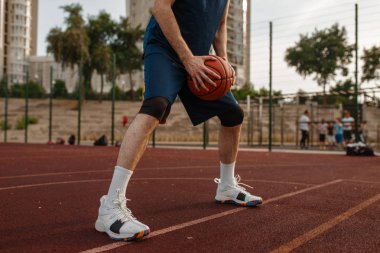 Erkek basketbolcu dışarıda bir top tutuyor. Spor giyimli erkek sporcu sokak topu antrenmanında, yaz stadyumunda.