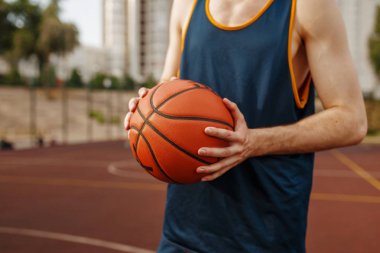 Basketbolcu açık hava sahasına atmayı hedefliyor. Spor giyim sektöründe erkek sporcu sokak topu antrenmanında topu tutuyor.